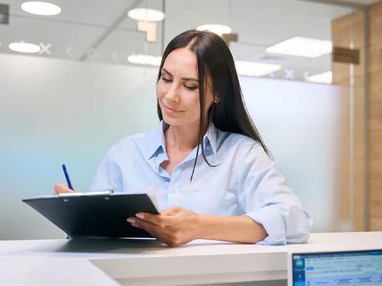 Woman sat in an office and writing on a clipboard