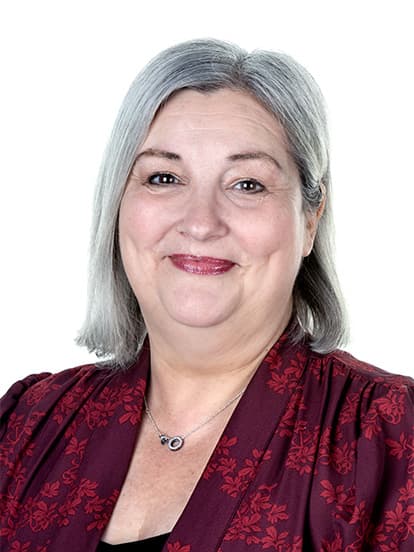 Smiling woman with gray hair, wearing a burgundy patterned blouse and a necklace