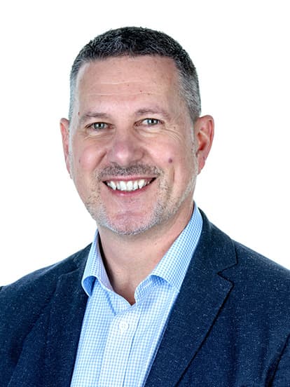 Smiling man with short gray hair, wearing a suit jacket and checkered shirt,