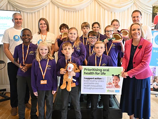 A group of children and adults, holding dental health props and a sign promoting oral health,