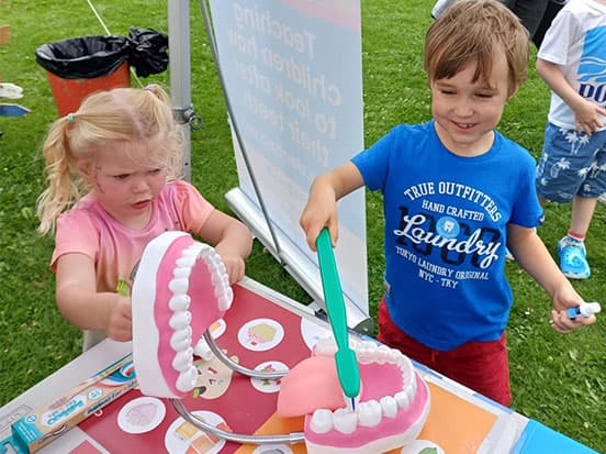 Two toddlers brushing a large model of teeth