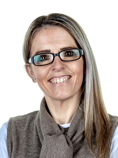 Smiling woman with long hair and glasses, wearing a white shirt and brown vest