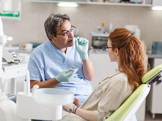 A professional dentist, equipped with a bright smile, converses with his red-haired female patient, carefully explaining the upcoming treatment, and ensuring her comfort throughout the process